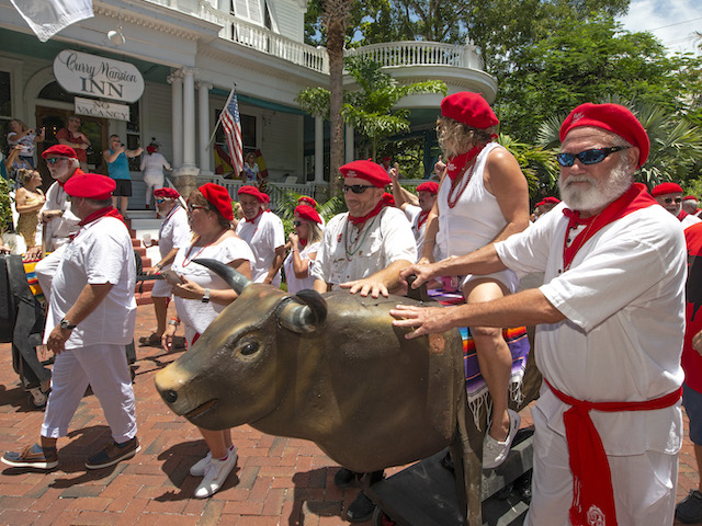 Ernest Hemingway look-alikes and others walk with manmade bulls on wheels during the “Running of the Bulls”