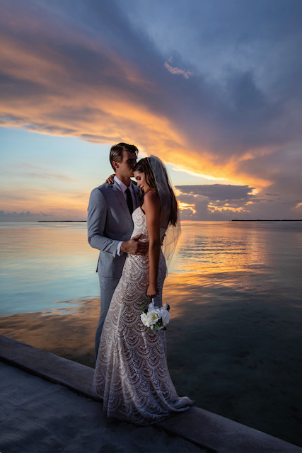 A bride and groom embrace by the ocean at twilight