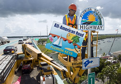 Rudy Nichols, a Florida Department of Transportation sign crew leader, positions a placard designating the Florida Keys Overseas Highway as an All-American Road, the highest national recognition a roadway can receive.
